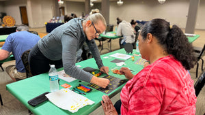 Anja Yamaji providing hands-on assistance to a student learing how to paint teardrop shapes on a practice sheet.