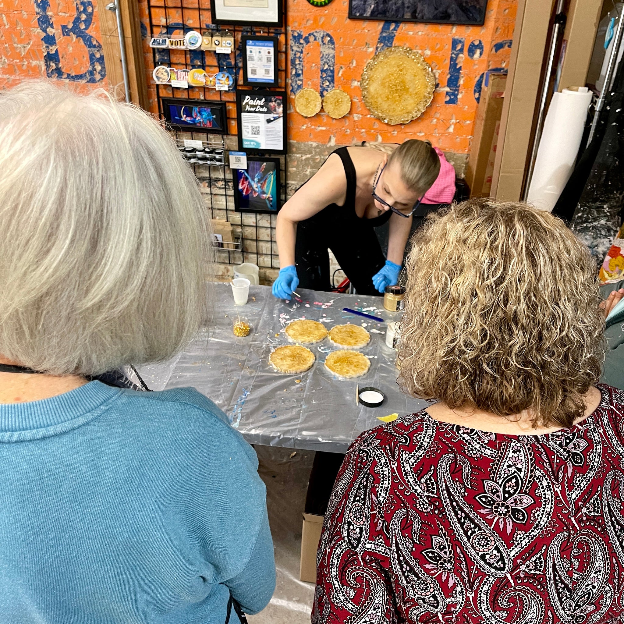 Anja Yamaji demonstrates how to use a toothpick to create a design in resin coasters as students watch her attentively.